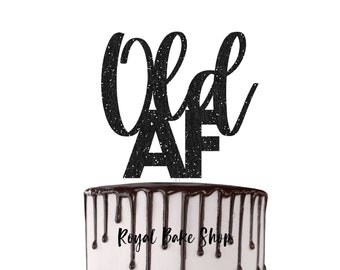 Könnte beinhalten: Schwarzer Glitzer-Kuchentopper mit dem Text "Old AF" auf einem weißen Kuchen mit Schokoladenüberzug.