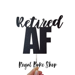 May include: Black glitter cake topper with the text "Retired AF" in a cursive font. The topper is on a stick and is held by a hand. The text "Royal Bake Shop" is visible in the bottom right corner of the image.