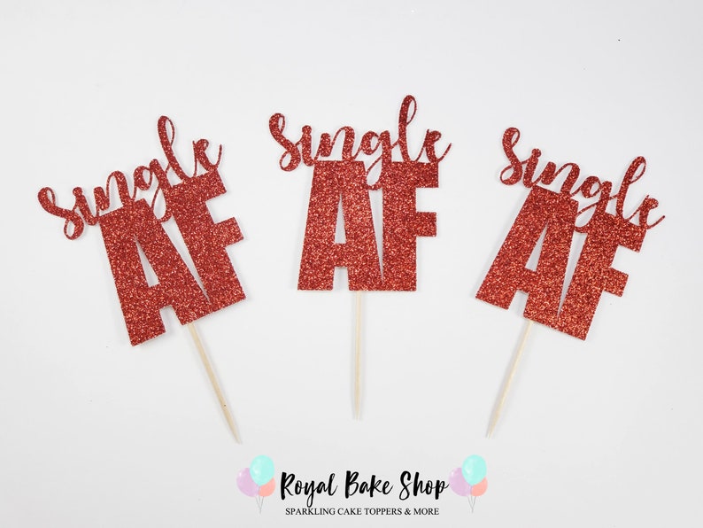 May include: Three red glitter cake toppers with the text "Single AF" on each. The toppers are on wooden sticks.