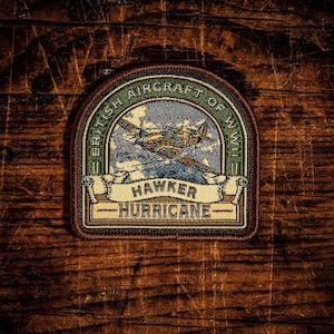 May include: A circular embroidered patch featuring a Hawker Hurricane aircraft flying through a cloudy sky. The border is green with the text BRITISH AIRCRAFT OF WWII. A cream-coloured banner at the bottom displays the text HAWKER HURRICANE.