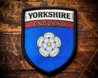 May include: A blue and white embroidered patch with the text "Yorkshire England" and a white rose with a yellow center.