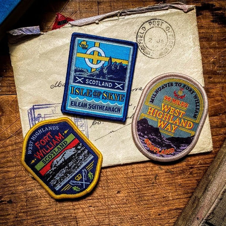 May include: Three embroidered patches featuring scenes from the Isle of Skye, Fort William, and the West Highland Way. The patches are on a brown paper background with a red and white stamp.