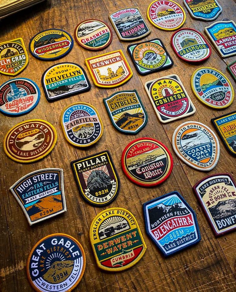 May include: A collection of colorful embroidered patches featuring various locations in the Lake District National Park in England. Each patch features a different mountain peak, lake, or town, along with the name of the location and its elevation in meters. The patches are made of a durable fabric and are perfect for adding a touch of personality to backpacks, jackets, or other items.