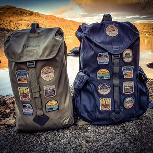 May include: Two large, green and blue backpacks with various patches and the word "Millican" on the front of the green backpack.
