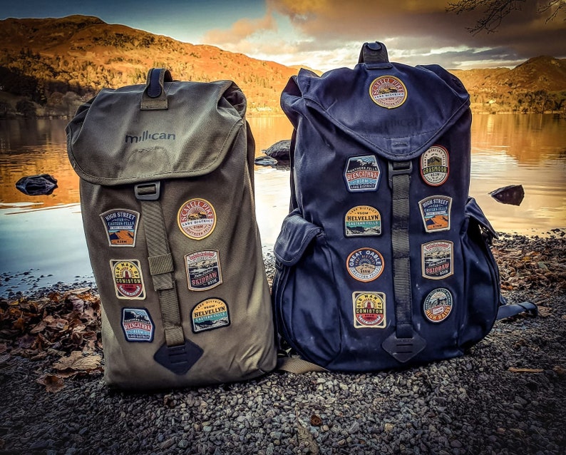 May include: Two large, green and blue backpacks with various patches and the word "Millican" on the front of the green backpack.