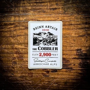 May include: White sticker with black text and a black and white illustration of a mountain. The text reads "Beinn Artair 884M The Cobbler Elev. 2,900 feet Scottish Carpatts Arrochar Alps".