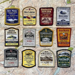 May include: A collection of embroidered patches featuring Scottish mountain names and elevations. Each patch has a unique design with text like "Ben Nevis" and "Cairn Gorm", and measurements in feet. The patches are on a map background.