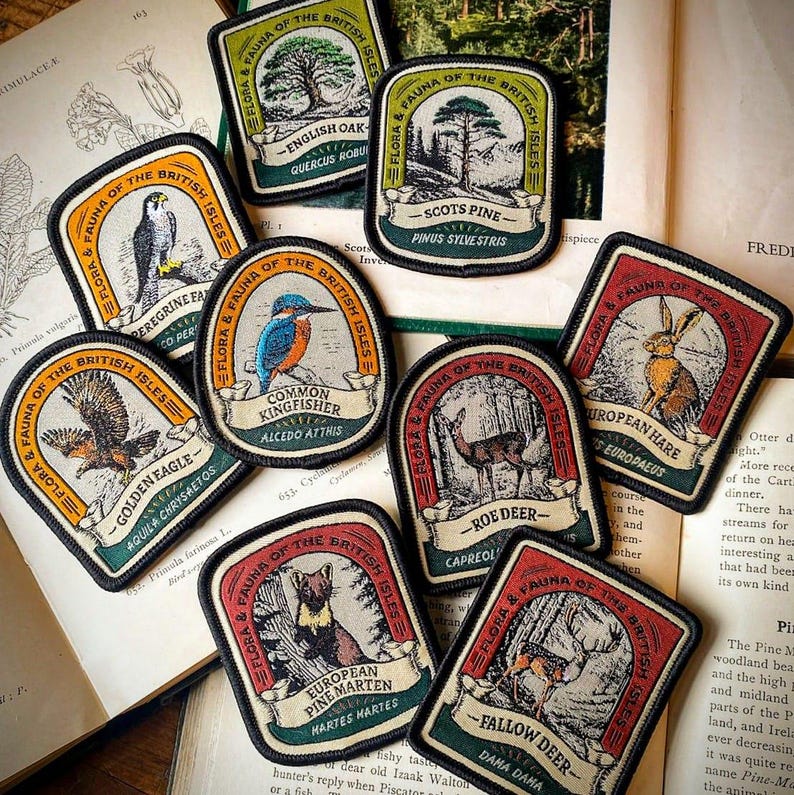 May include: A collection of eight embroidered patches featuring various flora and fauna of the British Isles. Each patch has a colorful design with a name and scientific name of the species depicted. The patches are on a brown book with text.