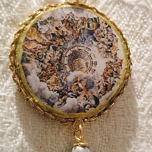 Immagine rappresenta il particolare centrale di uno degli orecchini. L'immagine rotonda è incorniciata da una piccola passamaneria in filo dorato.
Il dipinto raffigura il celebre affresco presente nel soffitto di Palazzo te a Mantova, dal titolo la Caduta dei Giganti