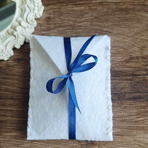 viene mostrato il pacchetto regalo che completa gli orecchini. Si tratta di un sacchetto di colori diversi e di materiale feltro rigido. Il sacchettino è chiuso con nastro in raso abbinato
