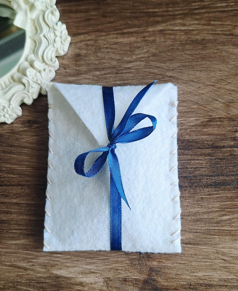 viene mostrato il pacchetto regalo che completa gli orecchini. Si tratta di un sacchetto di colori diversi e di materiale feltro rigido. Il sacchettino è chiuso con nastro in raso abbinato