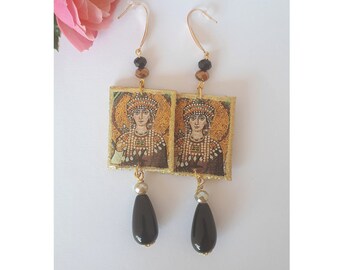May include: A pair of gold-toned drop earrings featuring rectangular pendants with a mosaic-style portrait of a figure in ornate headwear. Each earring includes black and metallic beads, a gold hook, and a smooth, black teardrop-shaped stone.