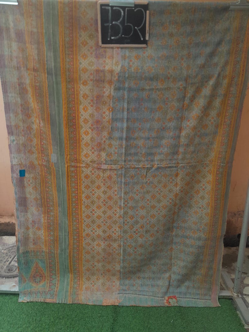 Puede incluir: Textil vintage con un dise&ntilde;o descolorido y estampado. La tela presenta una mezcla de colores, incluyendo azul, naranja y verde, con un patr&oacute;n geom&eacute;trico repetitivo. El texto "7352" es visible en una peque&ntilde;a pizarra adjunta al textil.