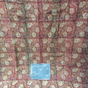 May include: A red and gold floral patterned fabric with a handwritten tag that says "63-73".