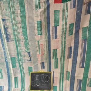 Puede incluir: Una alfombra tejida a rayas blancas, verdes, azules y rojas con un letrero negro de pizarra que dice "6580".