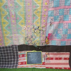 Puede incluir: Una colcha de retazos con una variedad de colores y patrones, incluyendo rosa, azul, amarillo y marr&oacute;n. La colcha est&aacute; hecha de diferentes telas cosidas juntas. Un peque&ntilde;o letrero de pizarra con el precio "7000" escrito en &eacute;l est&aacute; delante de la colcha.