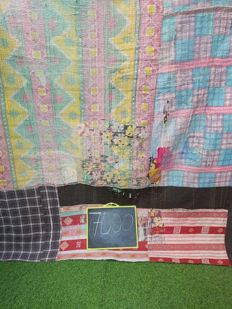 Puede incluir: Una colcha de retazos con una variedad de colores y patrones, incluyendo rosa, azul, amarillo y marr&oacute;n. La colcha est&aacute; hecha de diferentes telas cosidas juntas. Un peque&ntilde;o letrero de pizarra con el precio "7000" escrito en &eacute;l est&aacute; delante de la colcha.