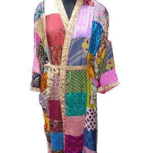 May include: A long, colorful patchwork robe with a sash tie. The robe is made of various fabrics in shades of pink, purple, blue, green, red, and yellow. The robe has a V-neck and long sleeves.