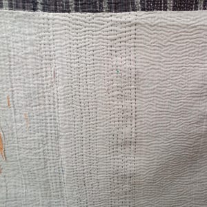 Puede incluir: Primer plano de una tela acolchada blanca con un patr&oacute;n de puntadas negras. La tela tiene una textura sutil y est&aacute; dividida en dos secciones por una costura vertical.