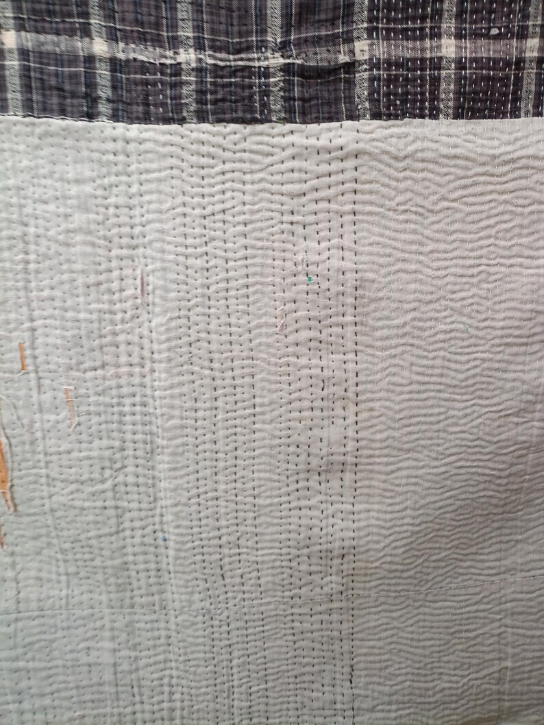 Puede incluir: Primer plano de una tela acolchada blanca con un patr&oacute;n de puntadas negras. La tela tiene una textura sutil y est&aacute; dividida en dos secciones por una costura vertical.