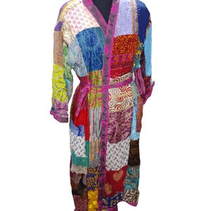 Pode incluir: Uma longa bata de patchwork colorida com uma faixa rosa. A bata é feita de diferentes tecidos e padrões, incluindo desenhos florais, paisley e geométricos.