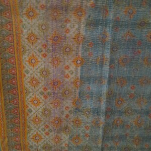 Puede incluir: Textil con un patr&oacute;n detallado en tonos azules, naranjas y morados. El dise&ntilde;o presenta formas florales y geom&eacute;tricas repetidas. Un borde con un patr&oacute;n de tri&aacute;ngulo repetido en naranja y verde recorre el lado izquierdo.