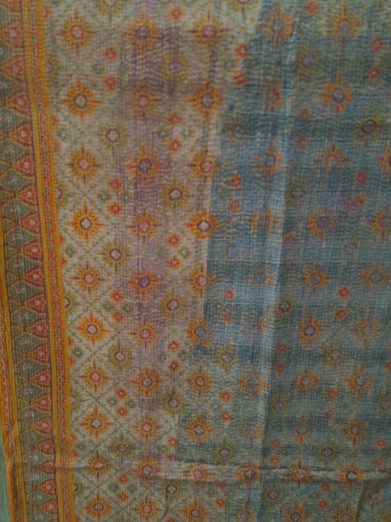 Puede incluir: Textil con un patr&oacute;n detallado en tonos azules, naranjas y morados. El dise&ntilde;o presenta formas florales y geom&eacute;tricas repetidas. Un borde con un patr&oacute;n de tri&aacute;ngulo repetido en naranja y verde recorre el lado izquierdo.