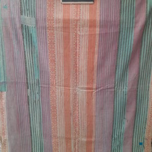 Puede incluir: Textil multicolor con rayas verticales en tonos naranja, morado y turquesa. La tela tiene un aspecto texturizado con una mezcla de rayas lisas y estampadas. Una peque&ntilde;a pizarra con el n&uacute;mero "7352" est&aacute; en la esquina superior derecha.