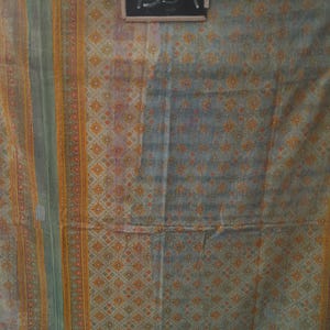 Puede incluir: Textil con un patr&oacute;n geom&eacute;trico repetitivo en tonos grises, naranjas y verdes. La tela tiene un aspecto descolorido, con un dise&ntilde;o central de peque&ntilde;as flores naranjas. El n&uacute;mero "7352" est&aacute; escrito en una peque&ntilde;a pizarra.