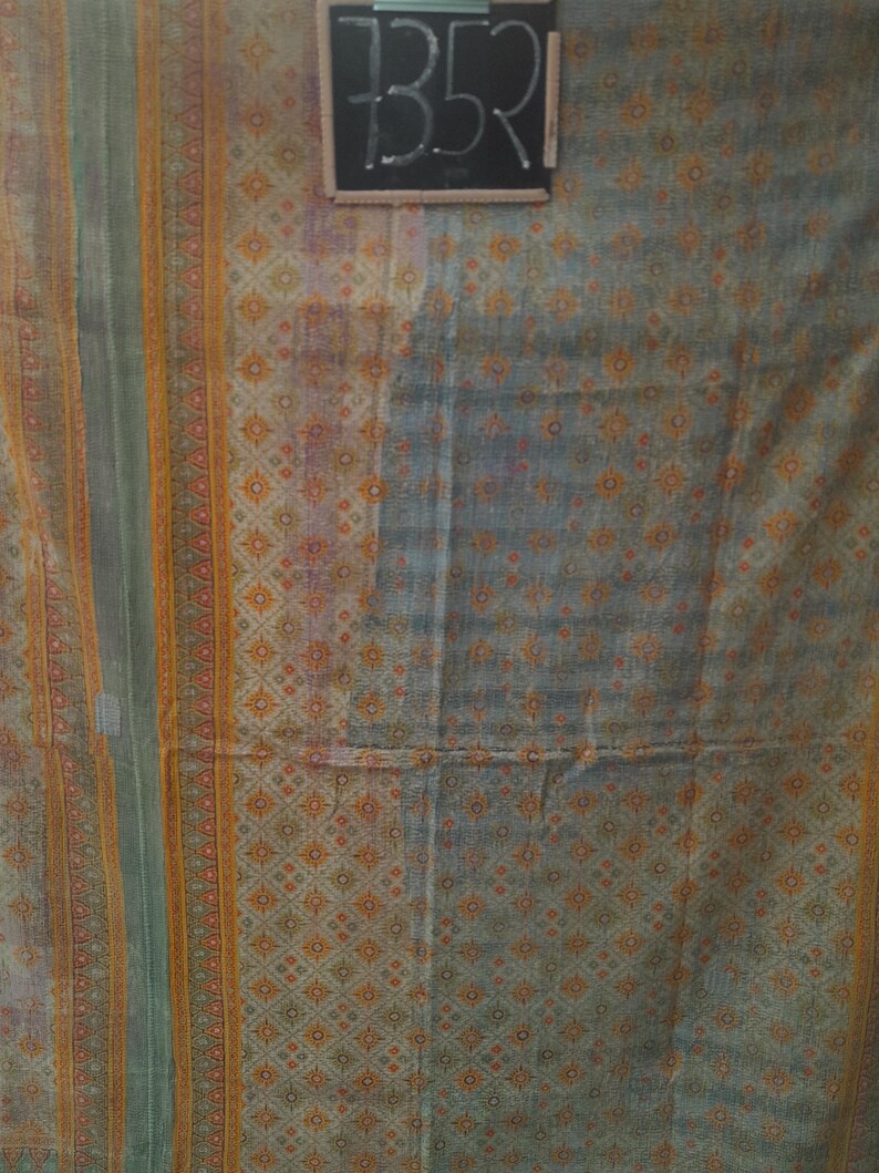 Puede incluir: Textil con un patr&oacute;n geom&eacute;trico repetitivo en tonos grises, naranjas y verdes. La tela tiene un aspecto descolorido, con un dise&ntilde;o central de peque&ntilde;as flores naranjas. El n&uacute;mero "7352" est&aacute; escrito en una peque&ntilde;a pizarra.