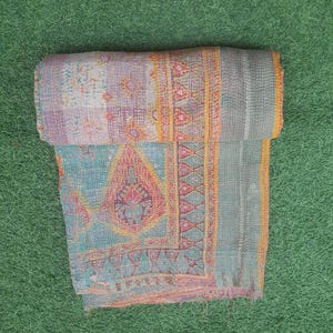 Puede incluir: Un edred&oacute;n plegado multicolor con patrones intrincados. El edred&oacute;n presenta un dise&ntilde;o de patchwork con tonos de azul, morado y naranja. Los bordes est&aacute;n adornados con un borde naranja contrastante. El edred&oacute;n est&aacute; hecho de una tela suave y texturizada.