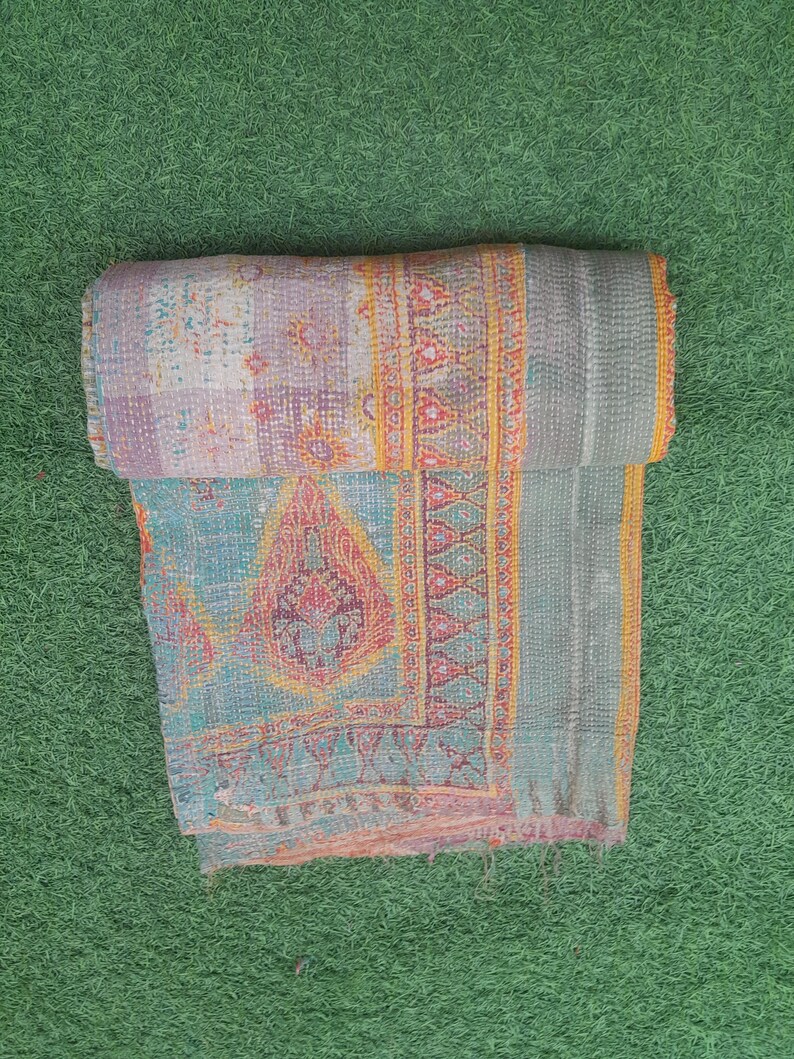 Puede incluir: Un edred&oacute;n plegado multicolor con patrones intrincados. El edred&oacute;n presenta un dise&ntilde;o de patchwork con tonos de azul, morado y naranja. Los bordes est&aacute;n adornados con un borde naranja contrastante. El edred&oacute;n est&aacute; hecho de una tela suave y texturizada.