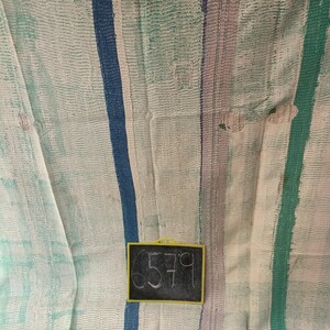 Puede incluir: Una colcha kantha blanca con rayas azules, verdes y moradas. La colcha tiene un diseño cosido a mano y está hecha de saris reciclados. Una pequeña pizarra con el número 6579 está en la esquina inferior derecha de la imagen.