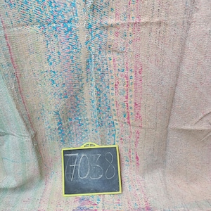 May include: A vintage kantha quilt with a blue, pink, and white pattern. The quilt is folded and has a chalkboard with the number 7038 written on it.