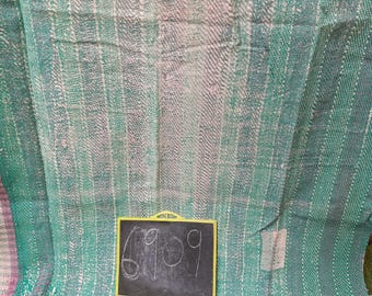 May include: A green and pink woven fabric with a frayed edge. A small black chalkboard with the number 6909 written on it is in front of the fabric.