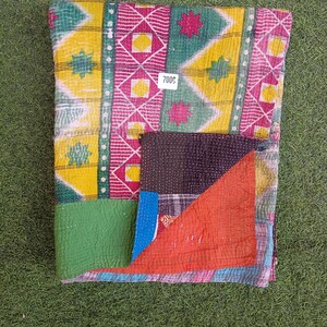 Puede incluir: Una colcha kantha colorida con un dise&ntilde;o de patchwork en telas verdes, amarillas, rosas y rojas. La colcha tiene un patr&oacute;n cosido a mano y est&aacute; doblada por la mitad. La etiqueta de precio dice "7000".