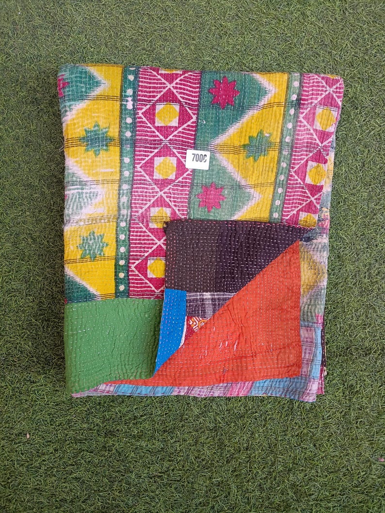 Puede incluir: Una colcha kantha colorida con un dise&ntilde;o de patchwork en telas verdes, amarillas, rosas y rojas. La colcha tiene un patr&oacute;n cosido a mano y est&aacute; doblada por la mitad. La etiqueta de precio dice "7000".