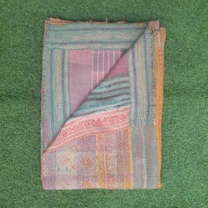 Puede incluir: Textil plegado multicolor con dise&ntilde;o de patchwork. El textil presenta una mezcla de tonos rosa, azul y amarillo, con costuras visibles y un aspecto texturizado. La esquina plegada revela la construcci&oacute;n en capas de la tela.