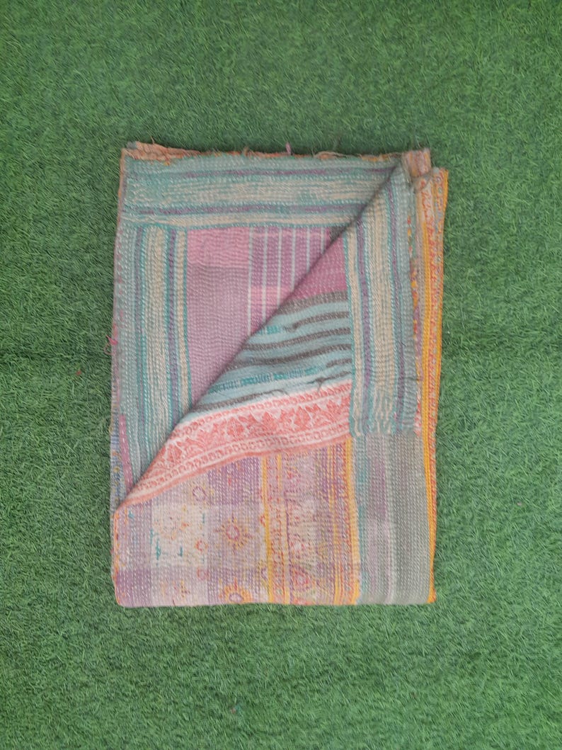 Puede incluir: Textil plegado multicolor con dise&ntilde;o de patchwork. El textil presenta una mezcla de tonos rosa, azul y amarillo, con costuras visibles y un aspecto texturizado. La esquina plegada revela la construcci&oacute;n en capas de la tela.