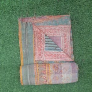 Puede incluir: Colcha patchwork plegada con una mezcla de colores que incluyen turquesa, rosa y morado. La colcha presenta intrincados patrones y dise&ntilde;os, con una secci&oacute;n enrollada en la parte inferior. La colcha est&aacute; colocada sobre una superficie verde.