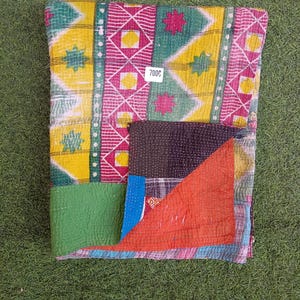 Puede incluir: Una colcha kantha colorida con un dise&ntilde;o de patchwork en telas verdes, amarillas, rosas y rojas. La colcha tiene un patr&oacute;n cosido a mano y est&aacute; doblada por la mitad. La etiqueta de precio dice "7000".