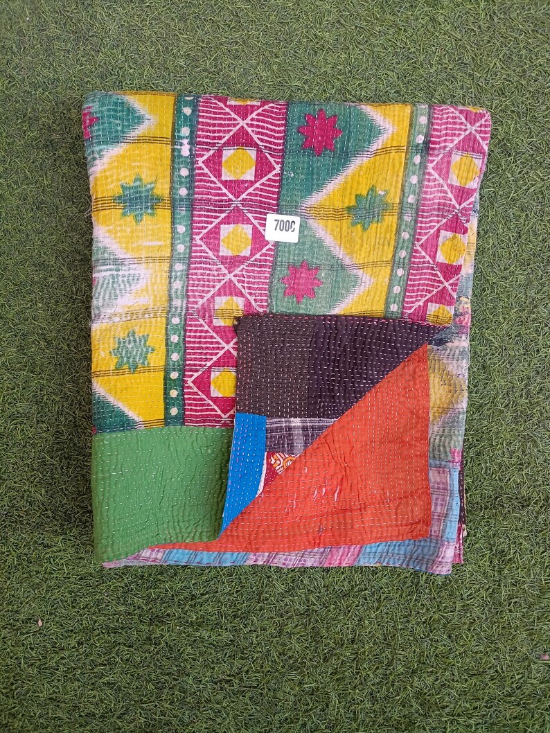 Puede incluir: Una colcha kantha colorida con un dise&ntilde;o de patchwork en telas verdes, amarillas, rosas y rojas. La colcha tiene un patr&oacute;n cosido a mano y est&aacute; doblada por la mitad. La etiqueta de precio dice "7000".