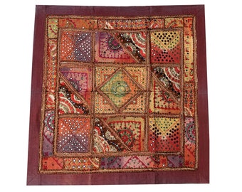 May include: A square patchwork throw pillow with a maroon border and intricate embroidery. The pillow is made of various fabrics in shades of red, orange, brown, and gold, with small mirror accents throughout.