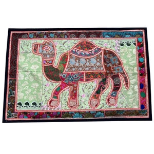 May include: A colorful patchwork wall hanging featuring a camel silhouette. The camel is made of various fabrics in shades of red, pink, green, blue, and brown. The background is a light green fabric with floral patterns.