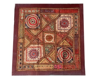 May include: A square patchwork quilt with a burgundy border. The quilt is made of various fabrics in shades of red, orange, yellow, green, and blue. The quilt is decorated with small mirrors and beads.