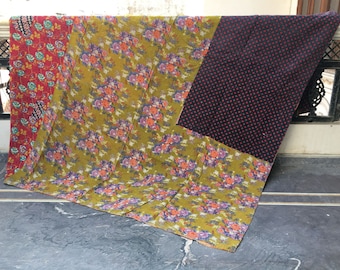 Op de afbeelding: Een patchworkdeken met drie panelen. Het grootste paneel is een groene bloemenprint, het op een na grootste is een zwarte stof met rode stippen en het kleinste paneel is een rode bloemenprint.