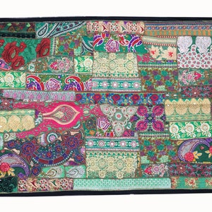 May include: A colorful patchwork wall tapestry with a green background. The tapestry is made of various fabrics and textures, including velvet, silk, and embroidery. It features intricate patterns and designs in shades of green, pink, purple, and gold.