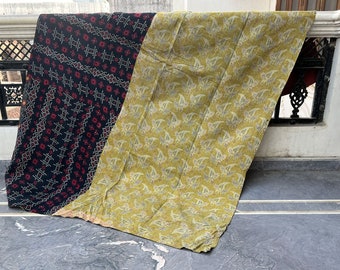 Op de afbeelding: Een vintage kantha-deken met een geometrisch patroon in zwart en rood aan de ene kant en een geel bloemenpatroon aan de andere kant.