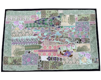 May include: A rectangular patchwork textile with a black border. The design features a variety of floral and paisley patterns in shades of green, pink, purple, and blue. The patches are sewn together with white stitching.