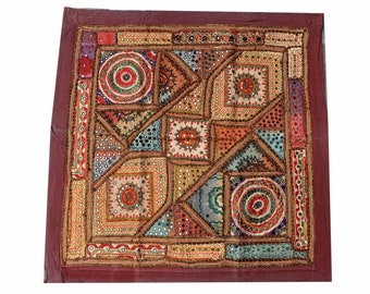 May include: A square patchwork quilt with a burgundy border. The quilt is made of various fabrics in shades of brown, red, green, blue, and gold. The quilt is decorated with small mirrors and intricate embroidery.